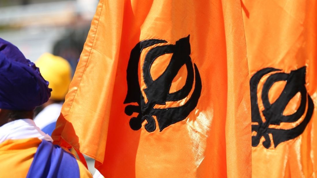 sikh man stands with two orange flags with khanda symbol on them